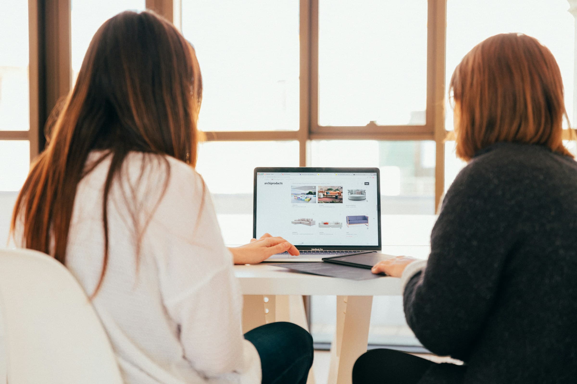 Twee mensen van achteren aan een tafel bij het raam, samen kijkend naar een laptop